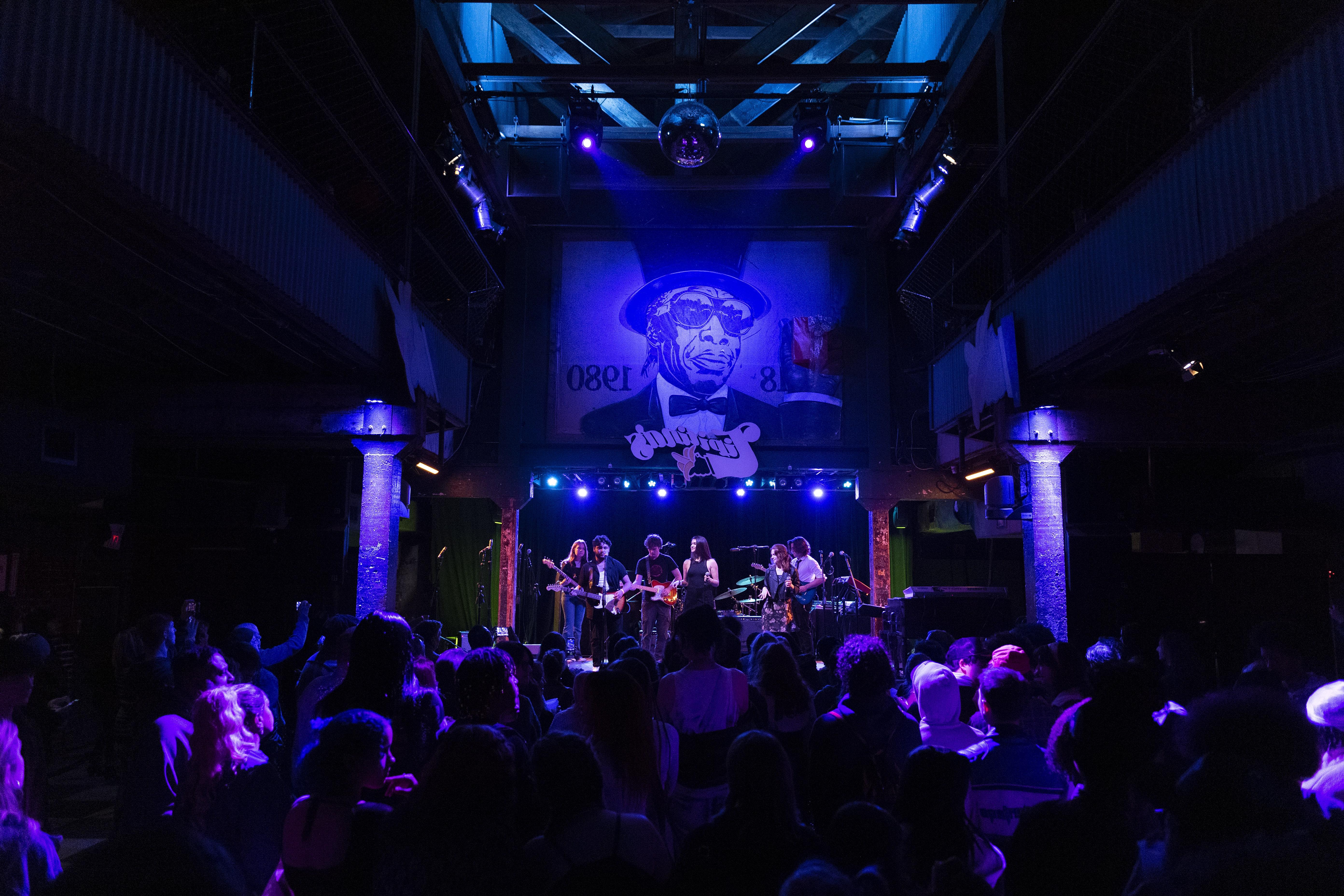 A full view of the Tipitina's concert venue, lit by soft blue light, with a Loyola band performing on stage.